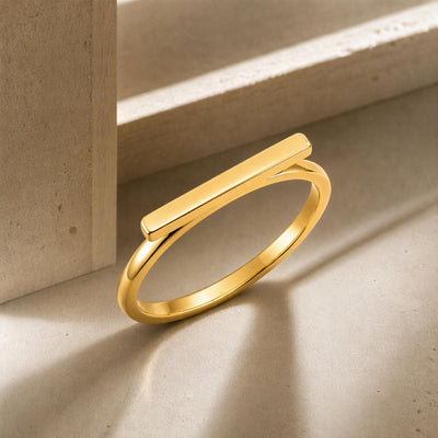14K gold horizontal bar ring propped against a stone ledge in sunlight