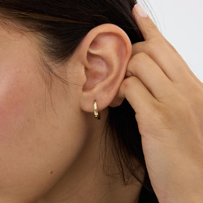 14K gold huggie hoop earring worn in the ear, close-up with a hand holding back the hair