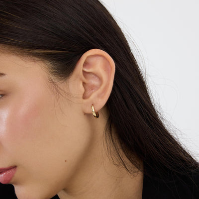 14K gold huggie hoop earring worn in the earlobe, side profile with dark hair