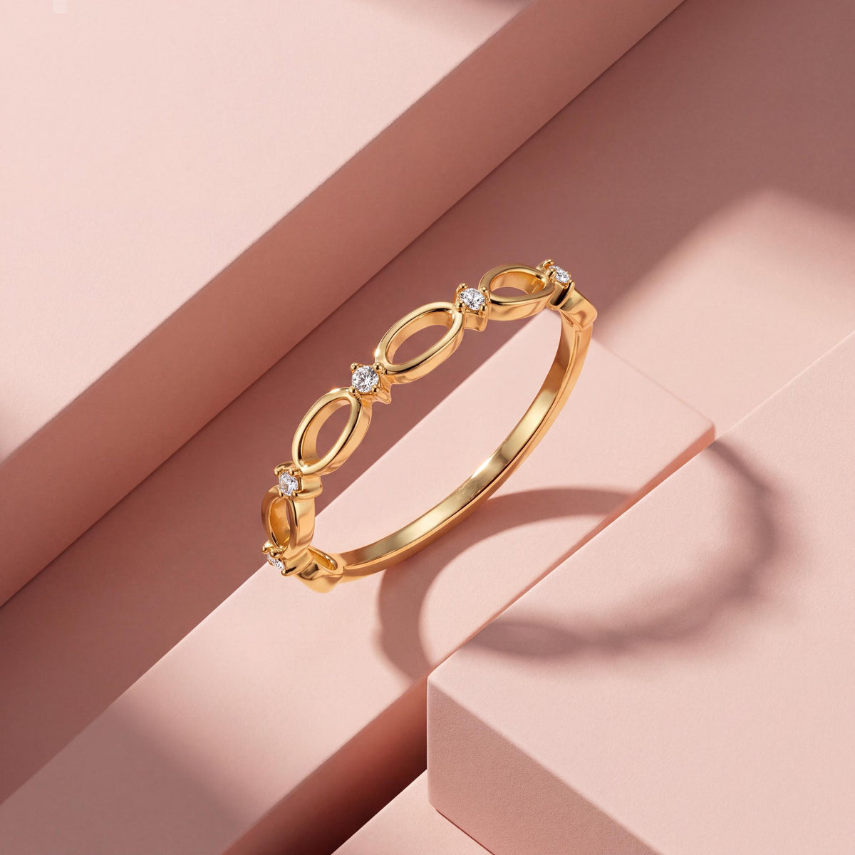 14K gold infinity ring with open oval links resting on pink geometric blocks with a hard shadow