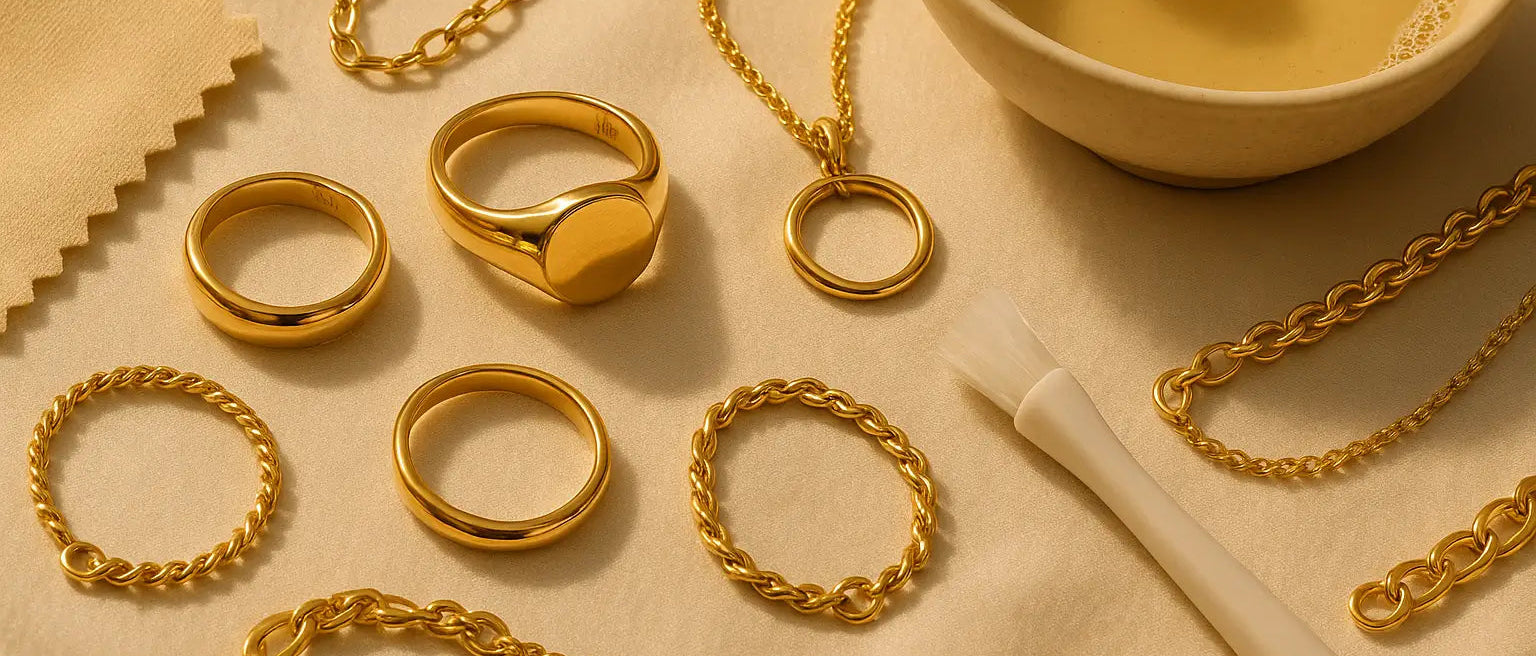 Gold jewelry including rings and chains on a beige surface with a bowl of liquid.