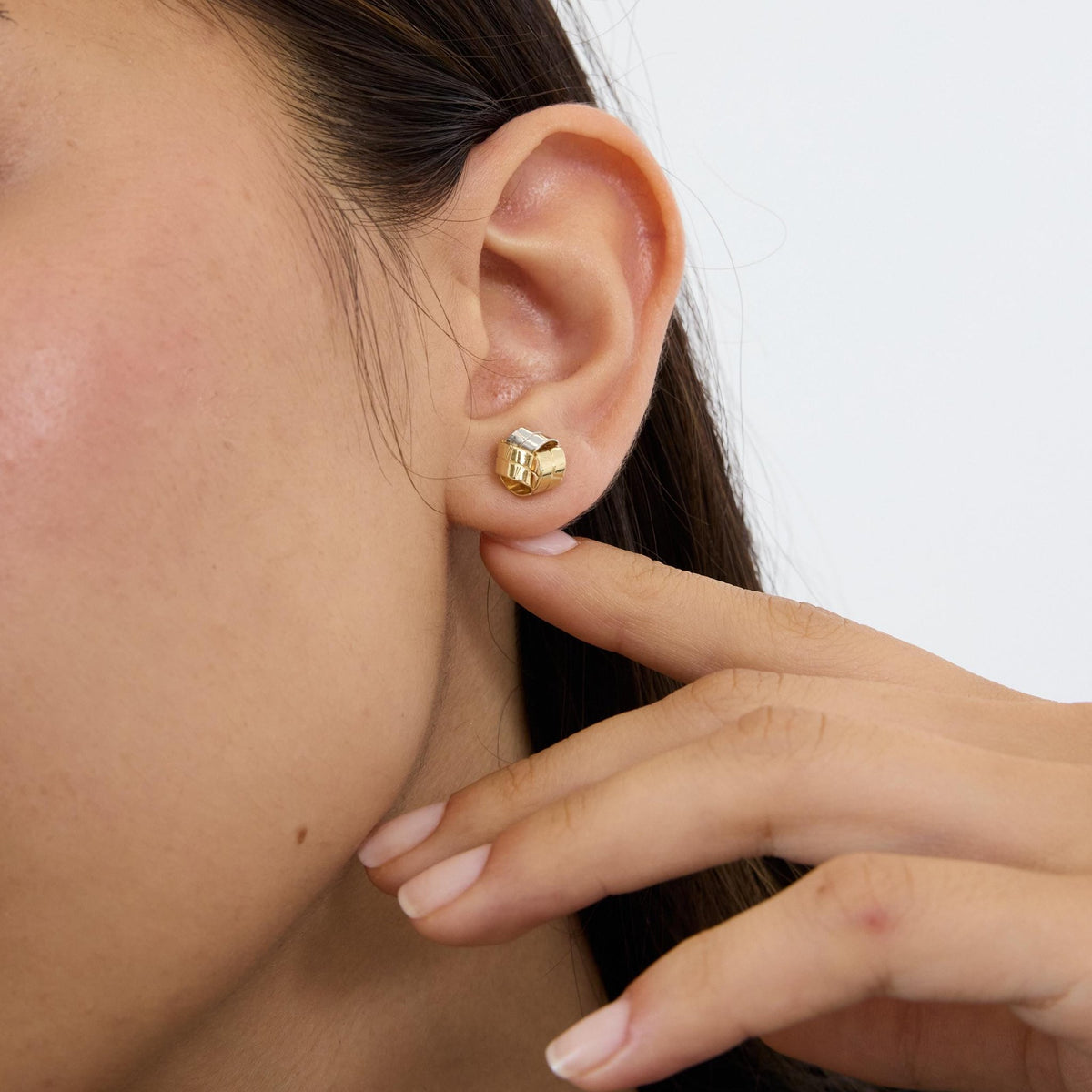 14K gold knot stud earring worn in ear, model touching earlobe with fingertip, side view