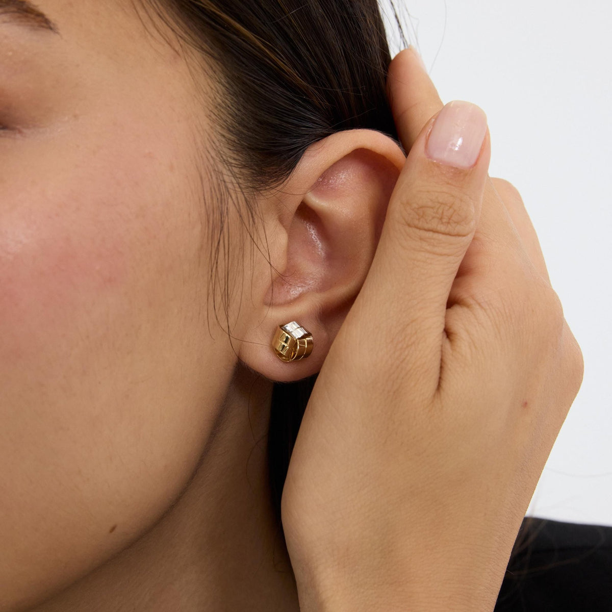 14K gold knot stud earring worn on ear, model holding hand behind ear, close-up