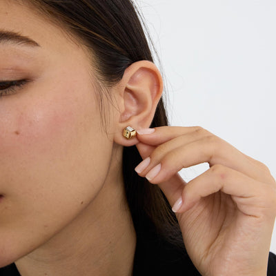 14K gold knot stud earring worn on earlobe, model's fingers near ear, three-quarter view