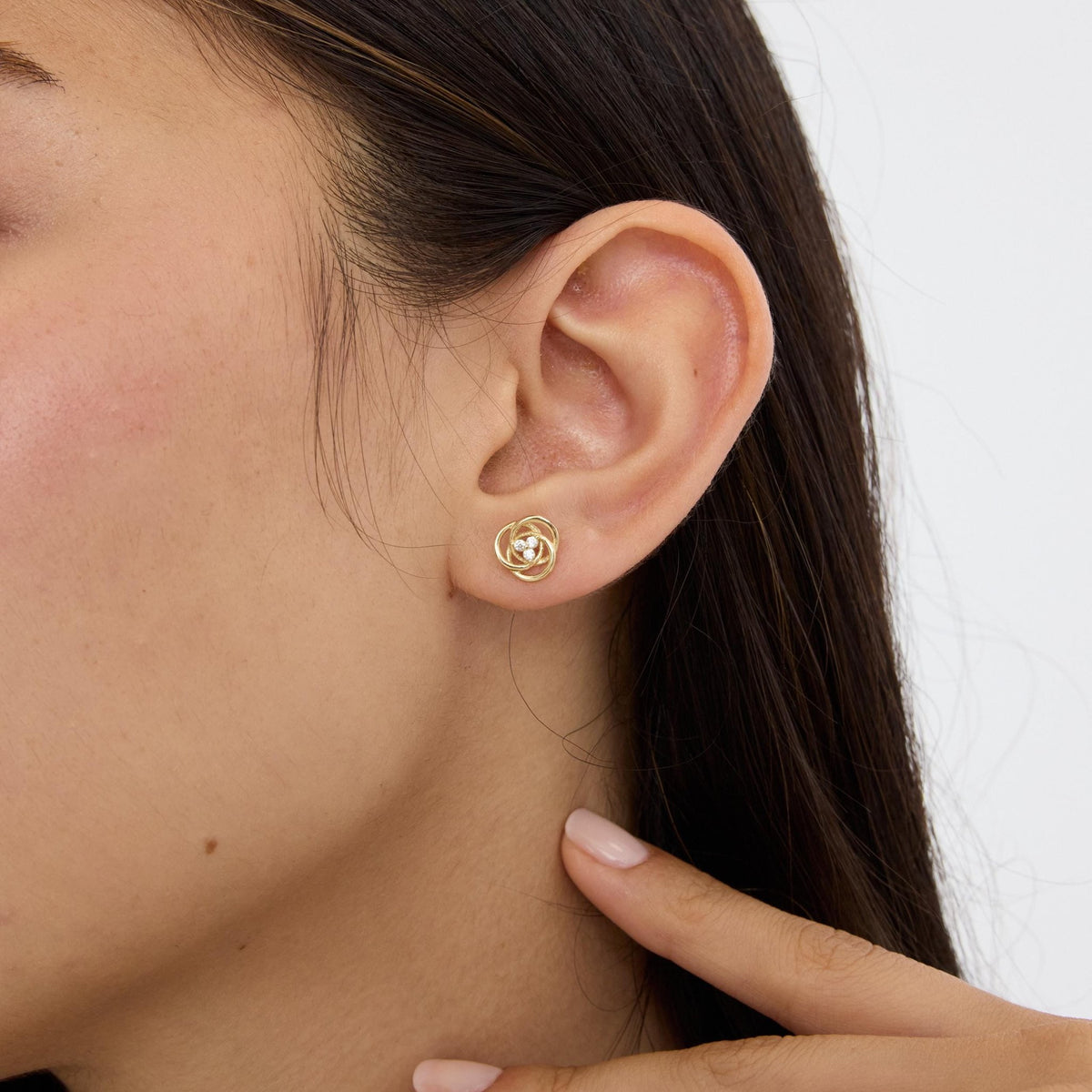 14K yellow gold love knot stud earring with cubic zirconia worn on ear, side profile with hand near neck