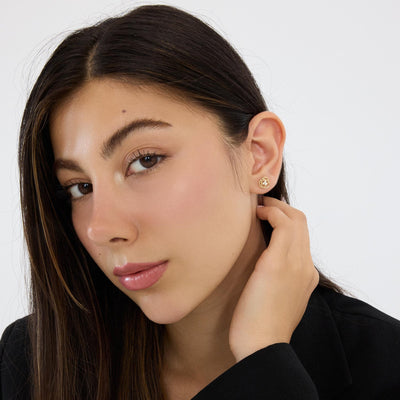 14K gold love knot stud earring with cubic zirconia worn by model with hand behind ear, portrait view