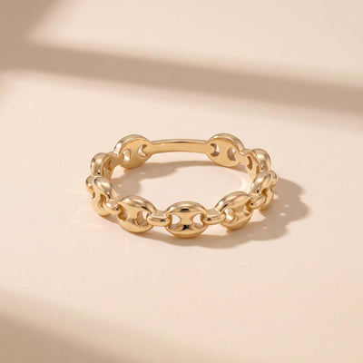 14K gold mariner link ring flat on pale surface with soft shadow, angled view