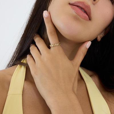 14K gold olive leaf ring worn on the index finger, hand resting under the chin
