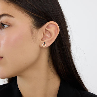 14K gold open circle stud earring with small black stone worn on ear, side profile of model with dark hair