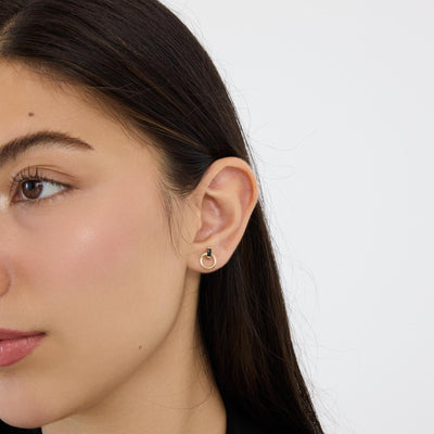 14K gold open circle stud earring with black stone worn in earlobe, close side view of model's face and ear