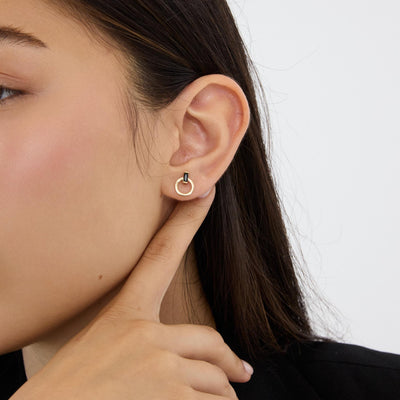 14K gold open circle stud earring with black stone, close-up on ear as model points a finger at the lobe