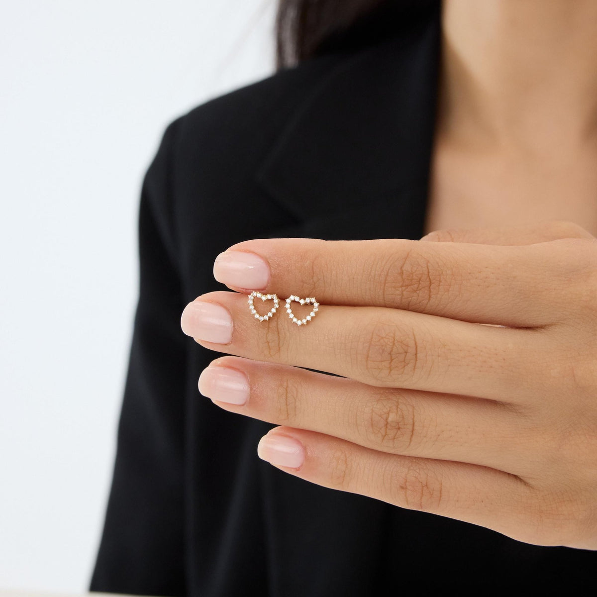 14K gold open heart stud earrings with cubic zirconia held on a woman's fingers to show small scale