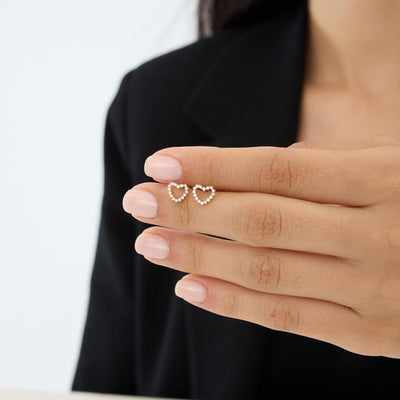 14K gold open heart stud earrings with cubic zirconia resting on fingertips, second hand-held angle