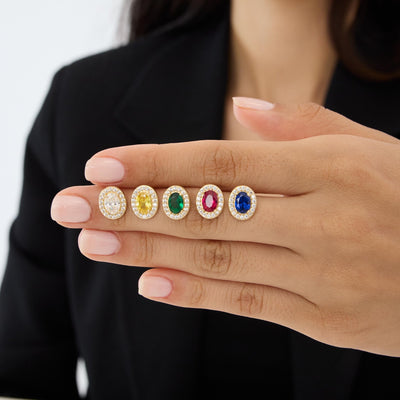 14K gold oval stud earrings in five stone colours resting on fingers, wider view of hand in black blazer