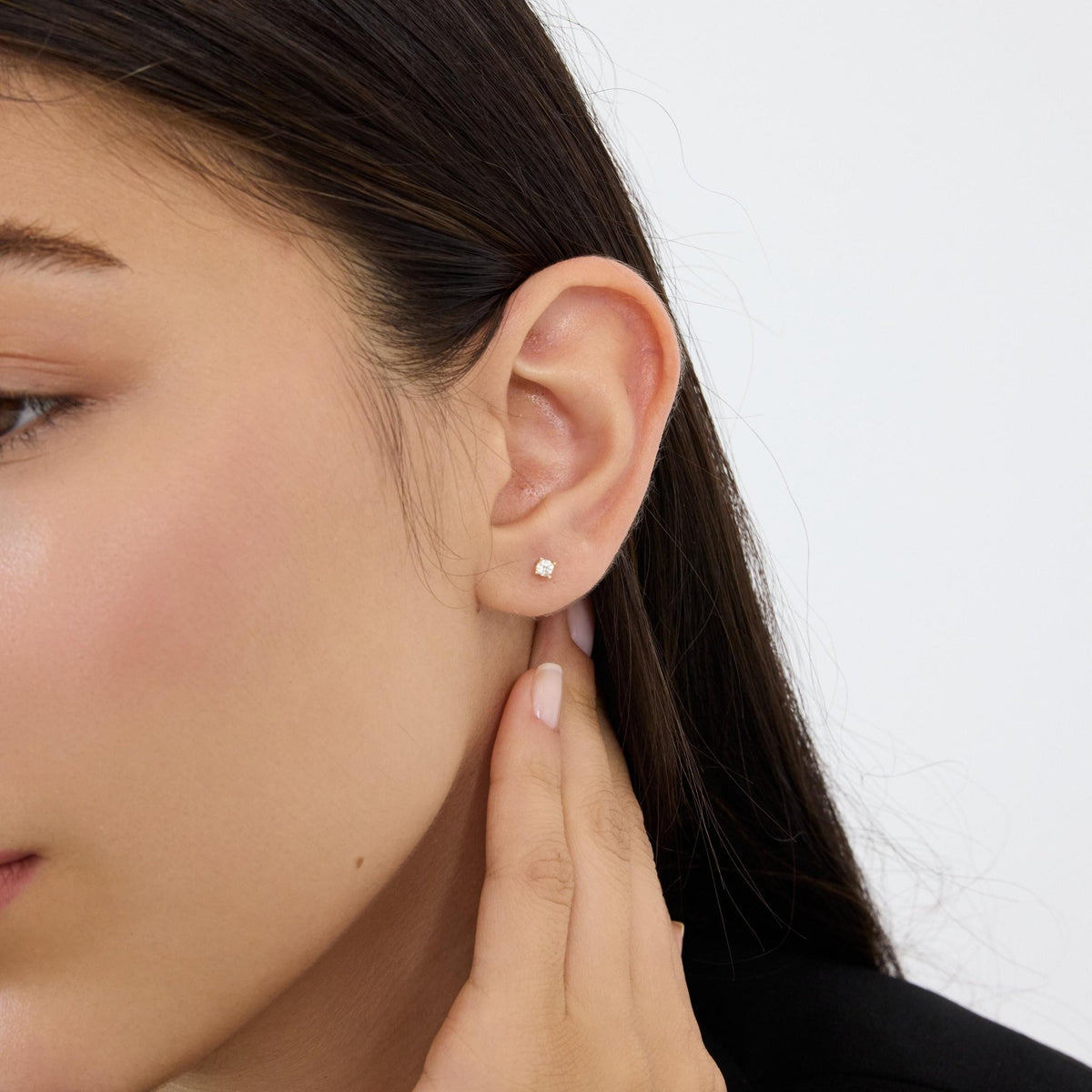 14K gold round cubic zirconia solitaire stud earring on the ear lobe, model's fingers at the jaw