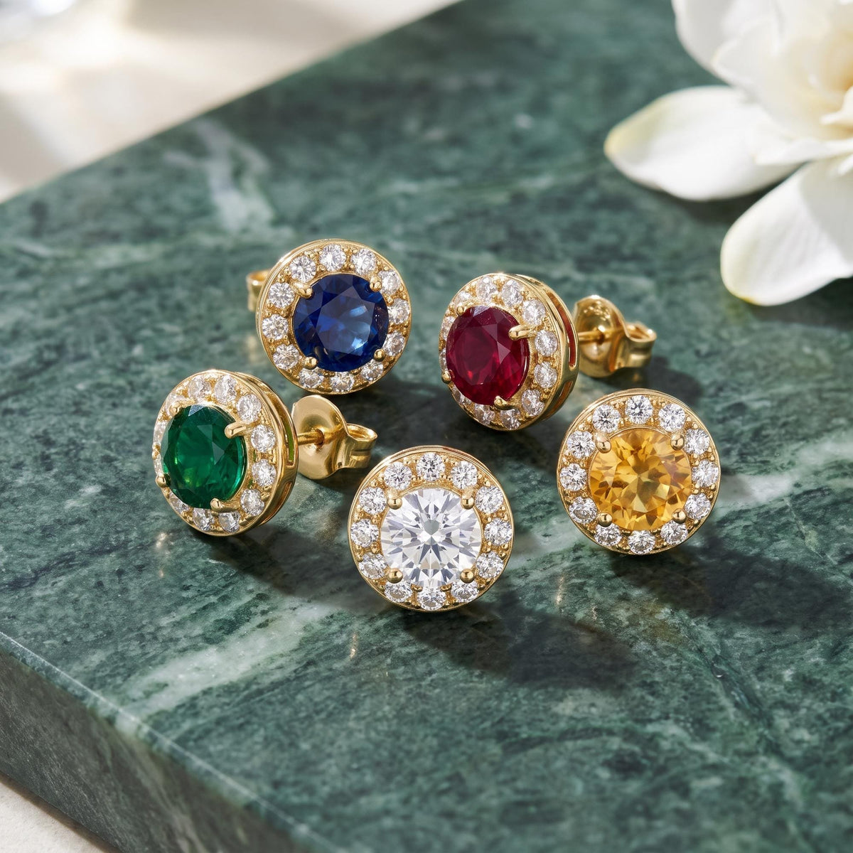 14K yellow gold round halo stud earrings in five stone options on green marble beside a white flower