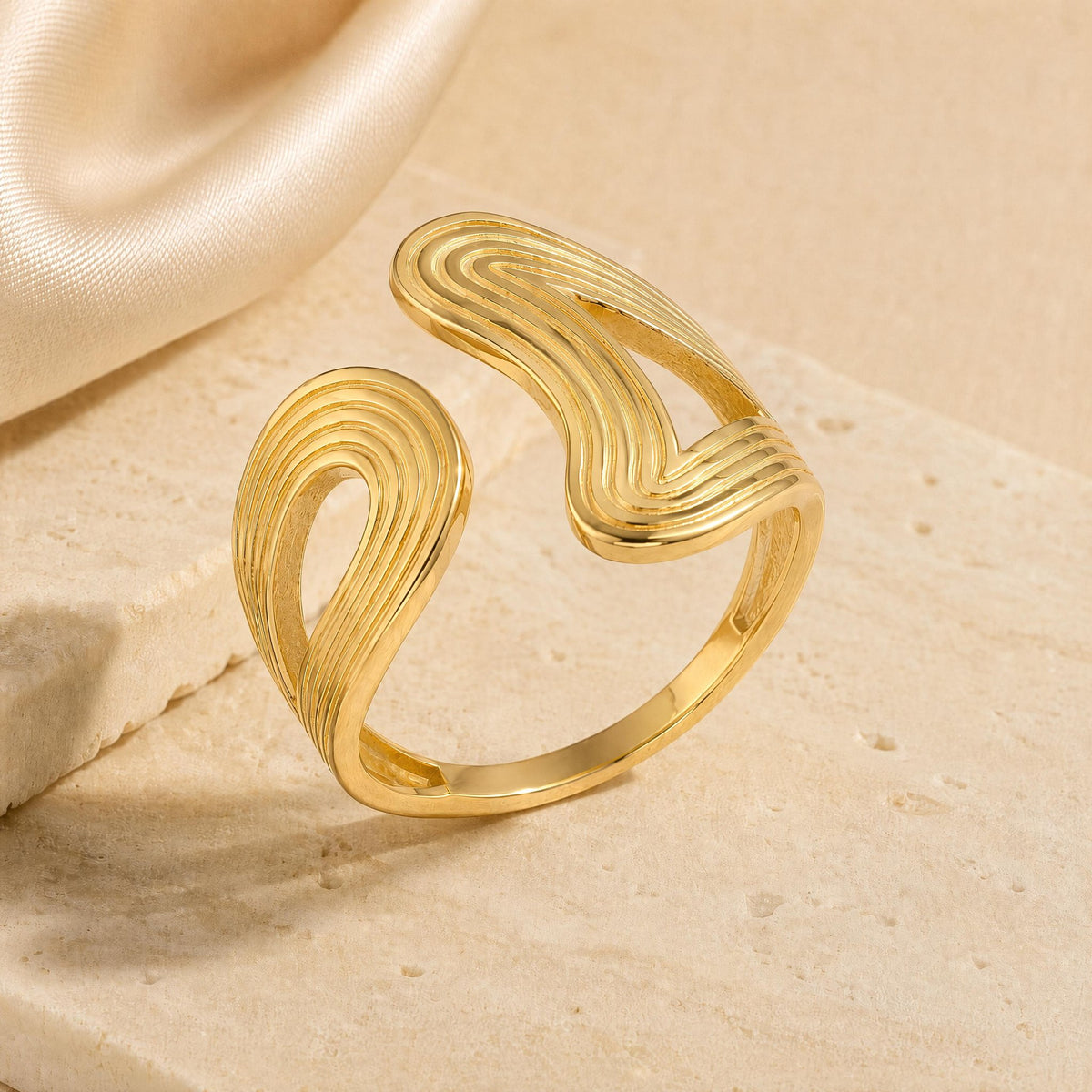 14K gold sculptural open ring with ribbed wave design on stone background
