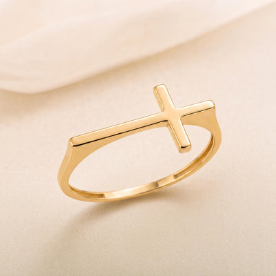 14K gold sideways cross ring on angled flat lay with soft draped fabric background