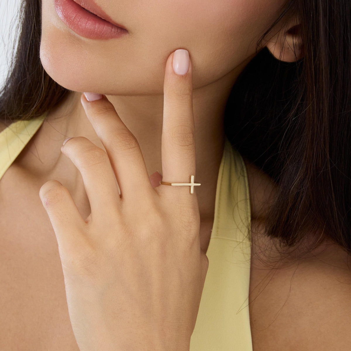 14K gold sideways cross ring close-up worn on finger touching model's chin