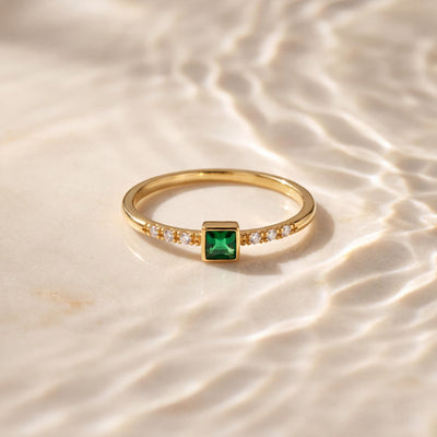 14K yellow gold square simulated emerald ring lying on a pale surface under rippling water light