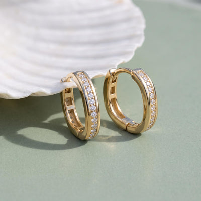 14K yellow gold square huggie hoop earrings with cubic zirconia, pair leaning on a white seashell