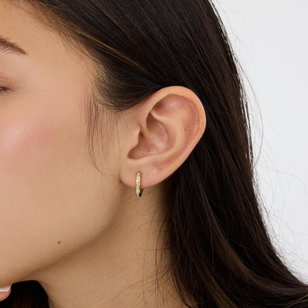14K gold square huggie hoop earring with cubic zirconia worn in a woman's ear, side profile view
