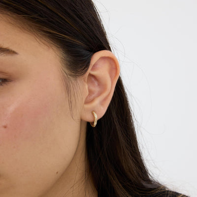 Close-up of 14K gold square huggie hoop earring with cubic zirconia on an ear, angled from the front