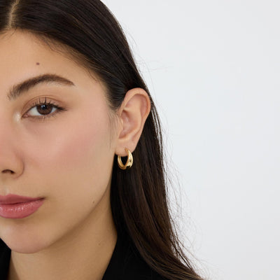 14K yellow gold tapered hoop earring worn on the ear while the model touches her hair behind it