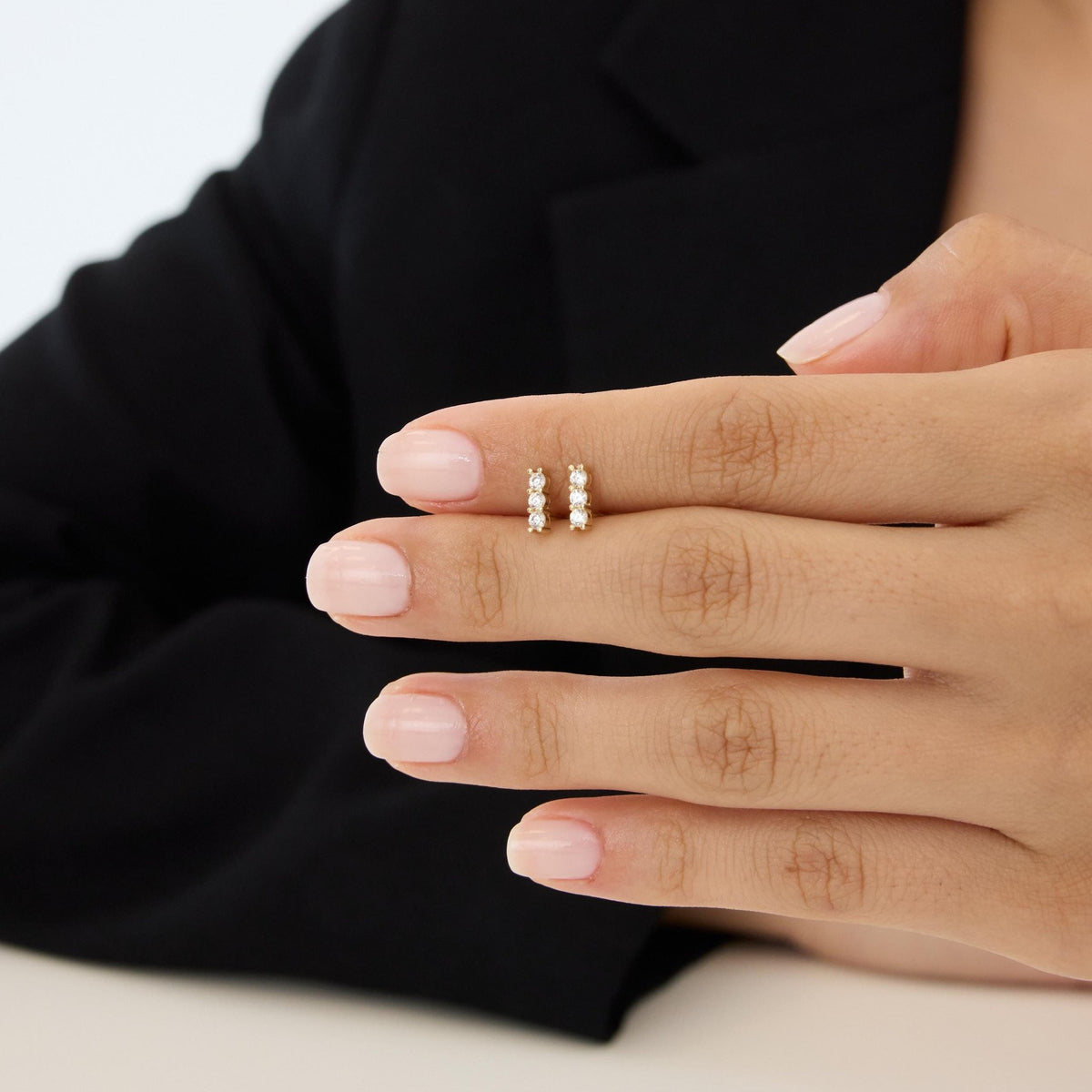 14K gold three stone cubic zirconia earrings, pair held on a hand with fingers to show tiny size