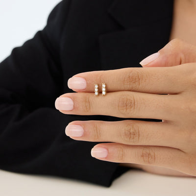 14K gold three stone cubic zirconia earrings, pair held on a hand with fingers to show tiny size