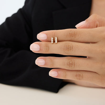 14K gold three stone cubic zirconia stud earrings, pair on fingers, second angle showing small scale