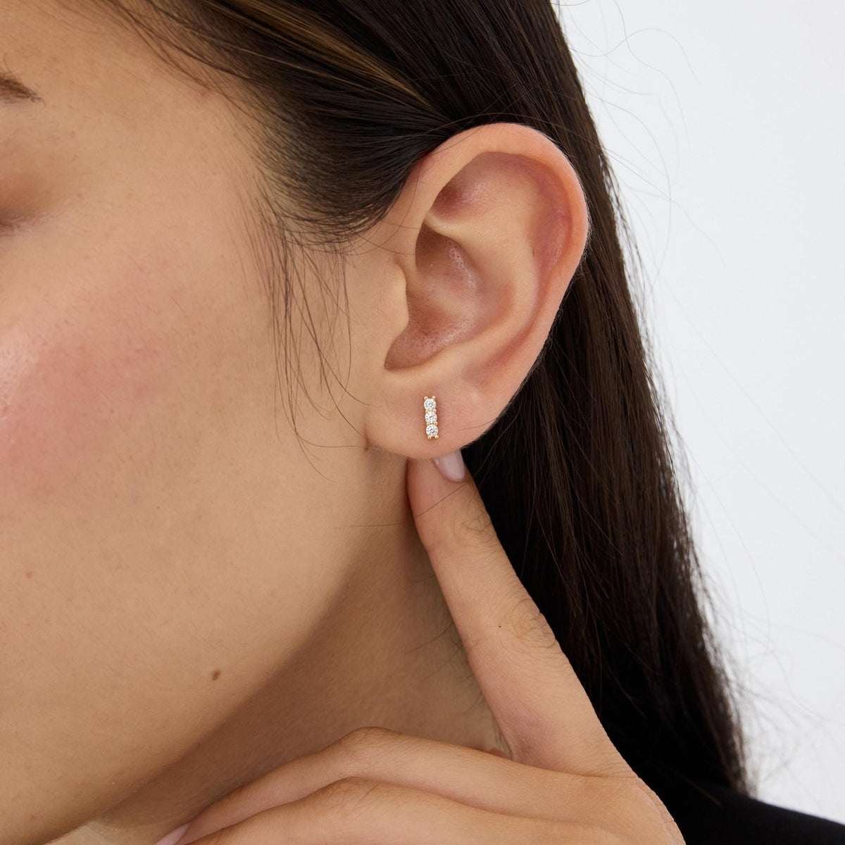 14K gold three stone cubic zirconia stud worn on the ear lobe, model touching neck, second angle