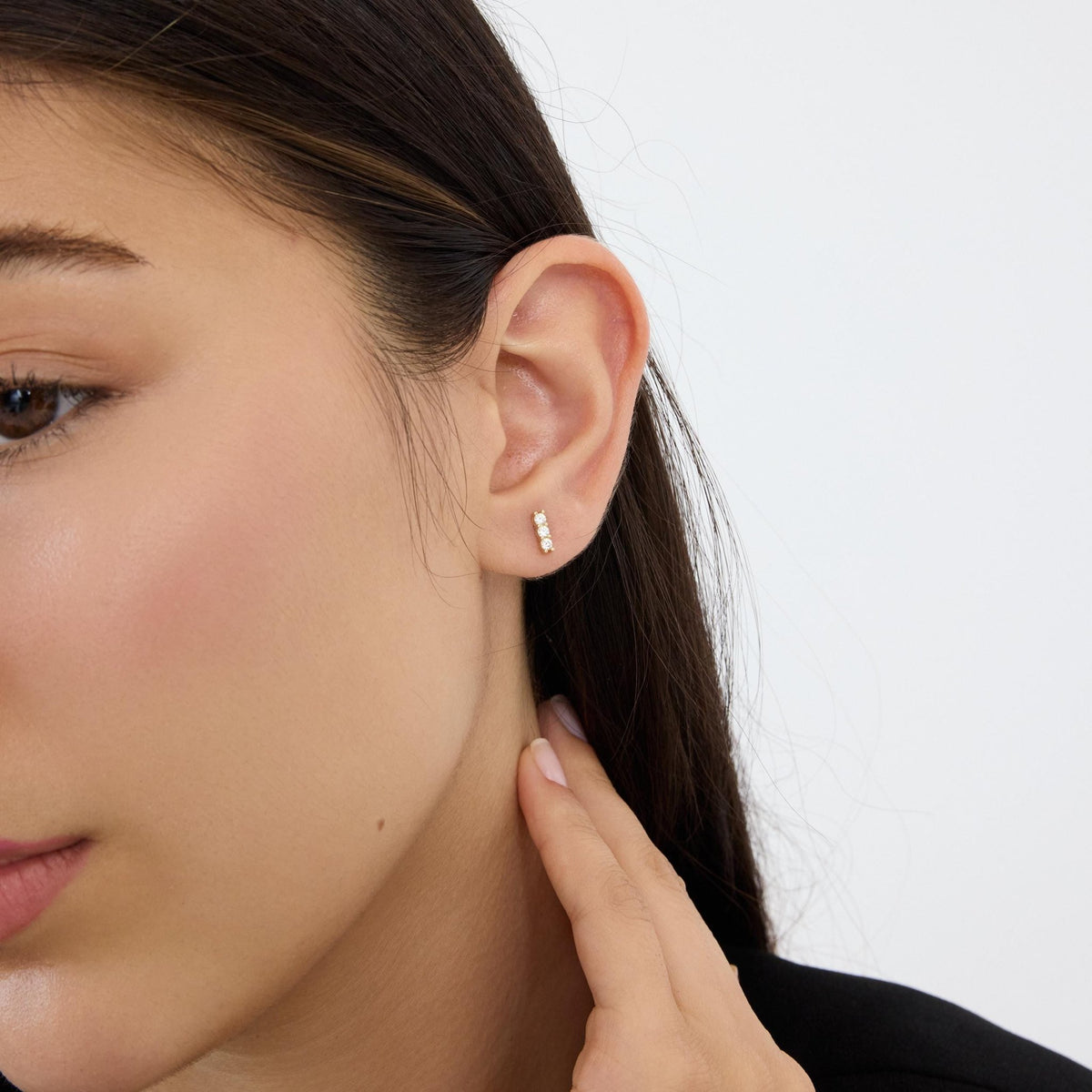 14K gold three stone cubic zirconia stud earring worn high on the ear, model's hand at neck
