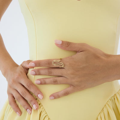 14K gold wave ring worn, hands resting at the waist of a pale yellow dress