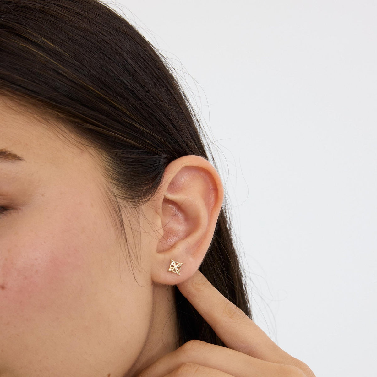 14K gold witch knot stud earring in an ear, close-up as the model touches below the earlobe